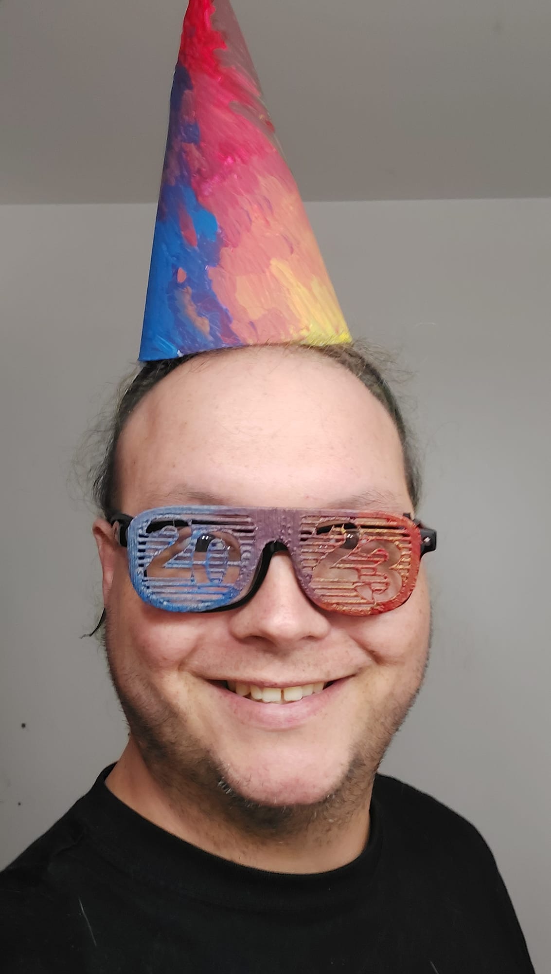 A man stands in the bathroom, wearing both the hat and painted glasses